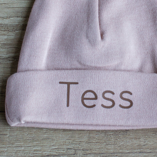 Close-up van gepersonaliseerd Pinkstone babymutsje met de naam Tess in chocoladebruine letters