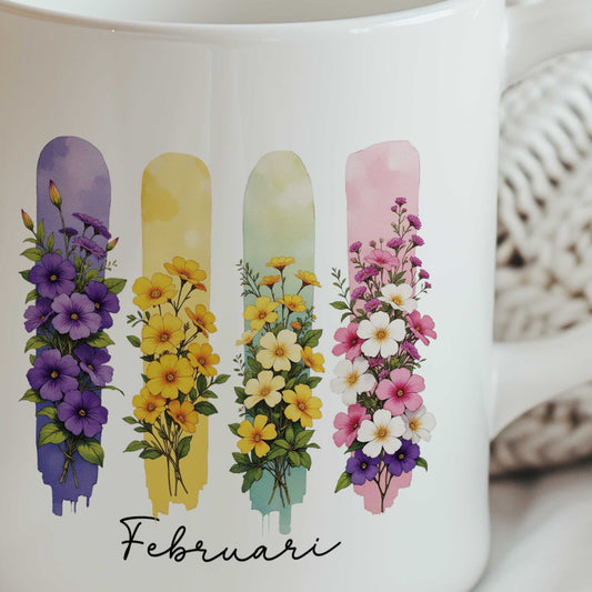 Close-up van een witte mok met de geboortebloemen van februari in brush effect, waarop de bloemenillustratie en de tekst 'Februari' duidelijk zichtbaar zijn.