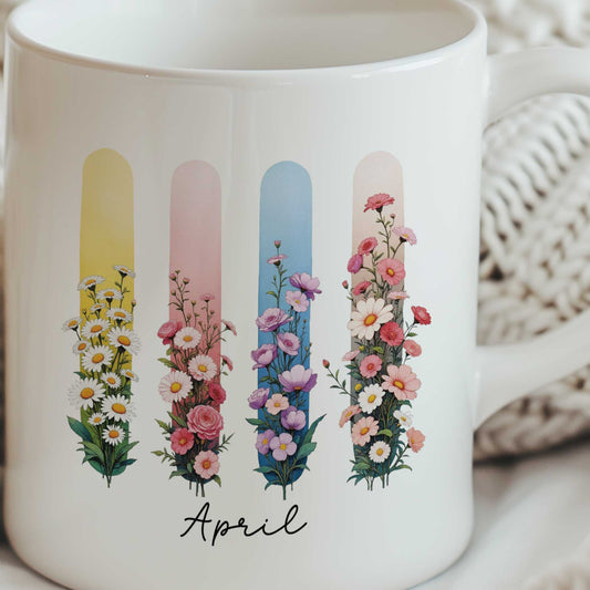 Close-up van een witte mok met illustratie van madeliefjes en lathyrus in een kleurrijk brush effect. De mok wordt met beide handen vastgehouden door een persoon in een witte gebreide trui tegen een lichtbeige geribbelde achtergrond.