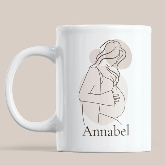 Witte gepersonaliseerde zwangerschapsmok met minimalistisch lijntekening ontwerp van een zwangere vrouw en de naam Annabel op een neutrale beige achtergrond.