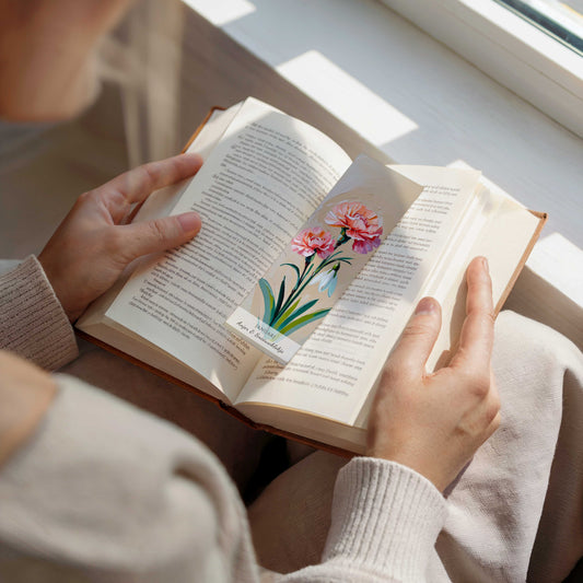 vrouw die een boek aan het lezen is met tussen de pagina's van het boek een boekenlegger met kunstzinnige illustratie van anjers en een sneeuwklokje