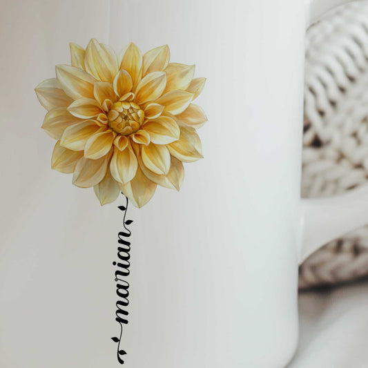Close-up van een witte mok met een gedetailleerde gele dahlia en een gepersonaliseerde naam die als bloemsteel onder de bloem is verwerkt.