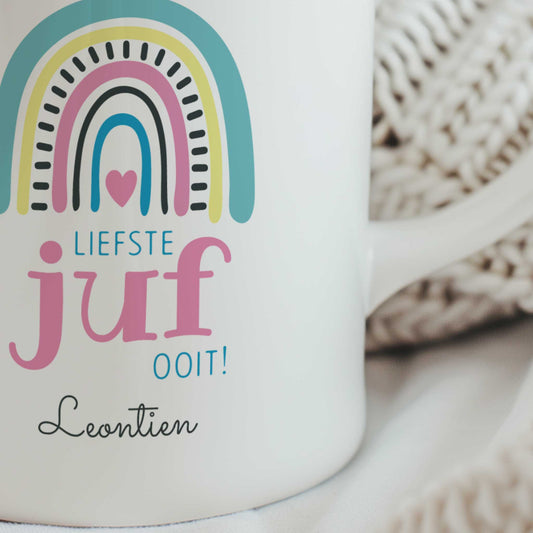 Close-up van witte juffenmok met pastel regenboog, tekst 'Liefste juf ooit!' en gepersonaliseerde naam onder het ontwerp