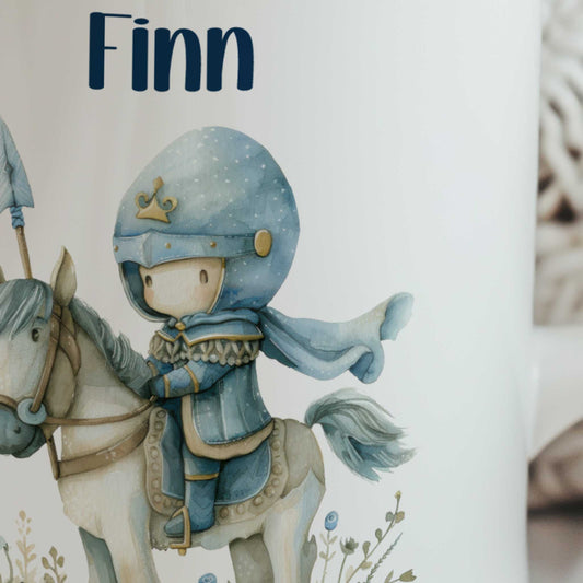 Close-up van een witte keramische mok met de naam Finn en een illustratie van een lieve blauwe ridder op een wit paard.