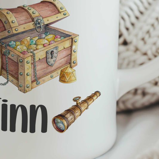 Close-up van een witte mok met een schatkist, een verrekijker en de naam Finn.