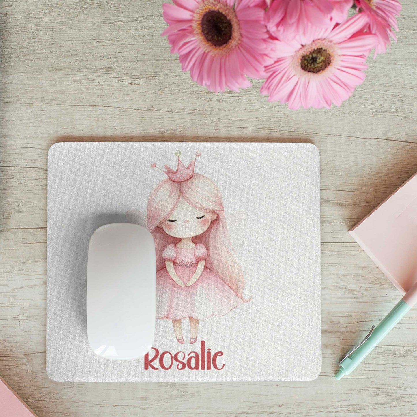Witte muismat met een prinses met roze kroontje en de naam Rosalie op een houten bureau. Naast de muismat liggen roze bloemen, een notitieboekje en een mintgroene pen.