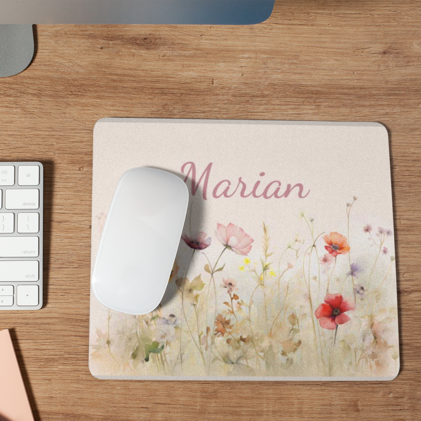 muismat met wilde bloemen tegen een zacht creme achtergrond met een naam in zachtroze. Naam is aanpasbaar. Muismat ligt op een houten bureau met een witte muis erop