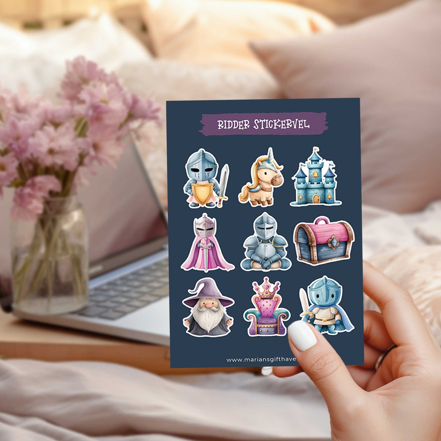 Hand houdt een ridder stickervel vast in een slaapkamer met roze bloemen, een laptop en zachte roze kussens op de achtergrond.