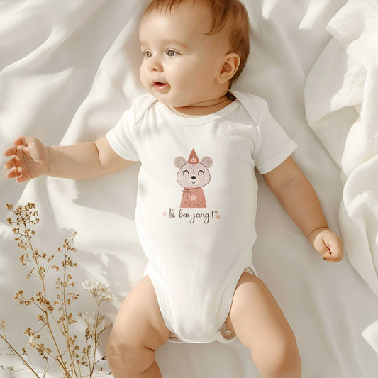 Baby draagt wit rompertje met muis-illustratie en tekst "Ik ben jarig!" terwijl hij op bed ligt