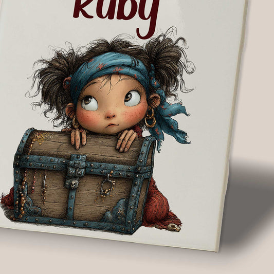Close-up van een keramisch tegeltje met de naam Ruby boven een illustratie van een klein piratenmeisje dat achter een houten schatkist vandaan kijkt.