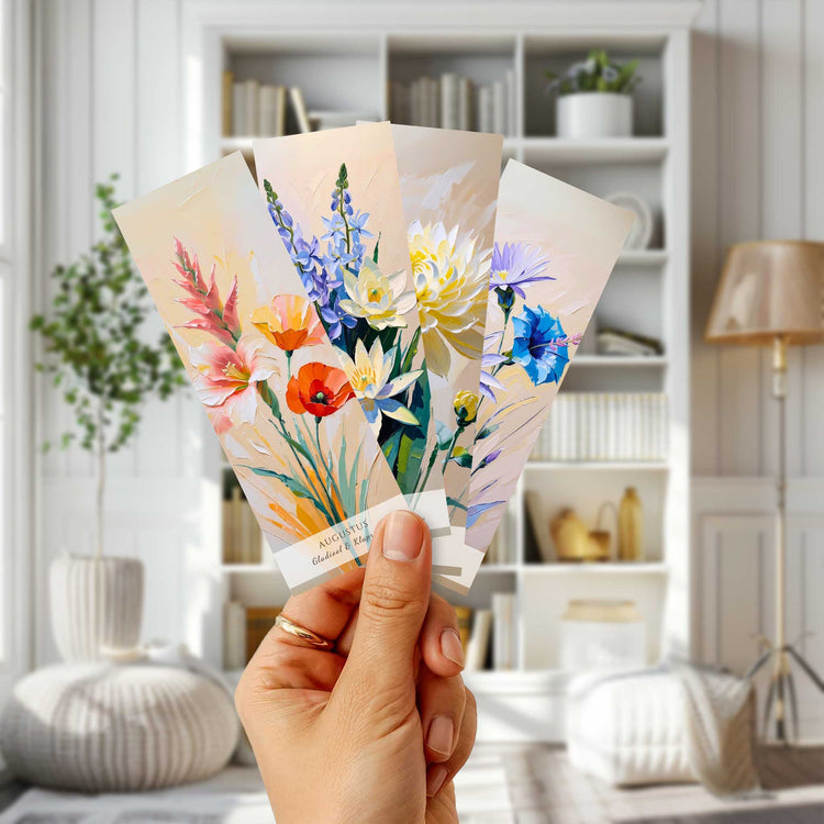 Hand met vier kleurrijke geboortebloem boekenleggers voor een witte boekenkast in een lichte woonkamer.