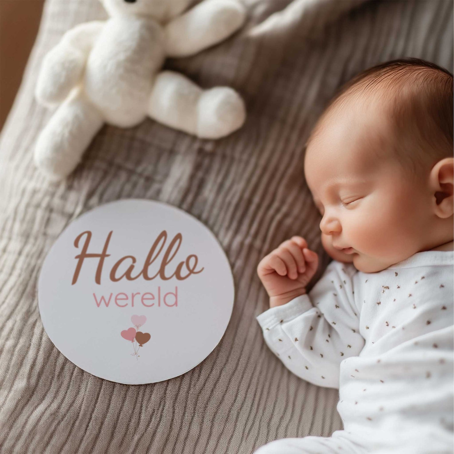Pasgeboren baby liggend op bed met mijlpaalschijfje 'Hallo wereld' naast de baby