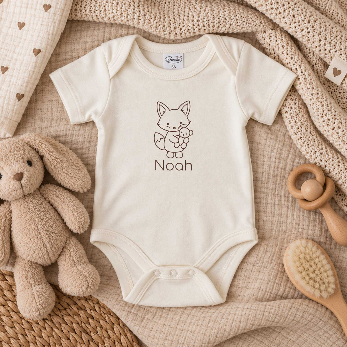 Ecru babyromper met gepersonaliseerd vosje en naam, liggend tussen zachte beige dekens met knuffel en houten accessoires