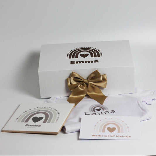 Witte cadeaudoos met naam Emma en regenboogprint met gouden strik, met daarvoor een wit babyrompertje met naam, keramisch tegeltje en kaartje op een witte achtergrond