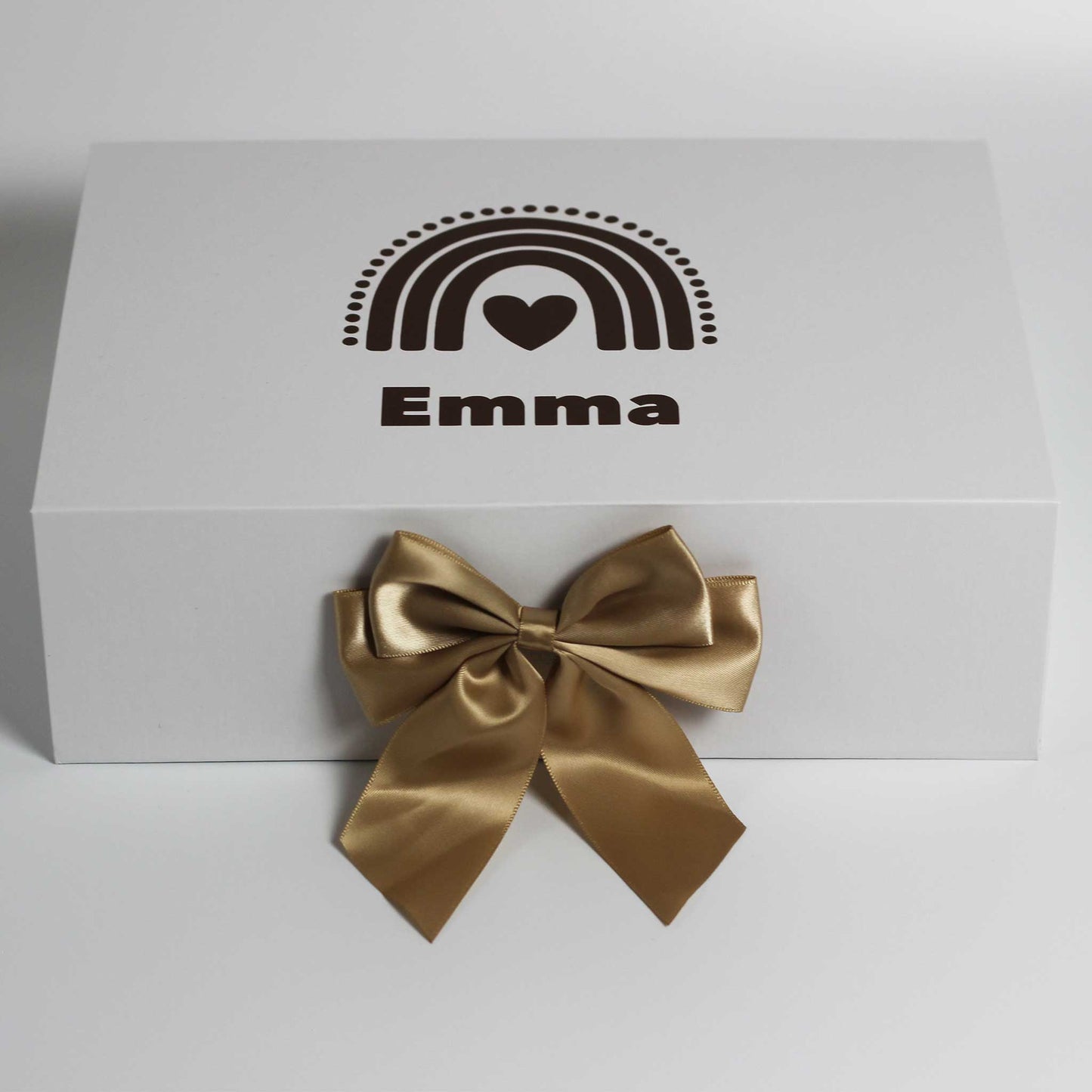 Witte cadeaudoos met een regenboog in donkere tinten en de naam Emma op de deksel, met een grote glanzende gouden strik aan de voorkant op een witte achtergrond