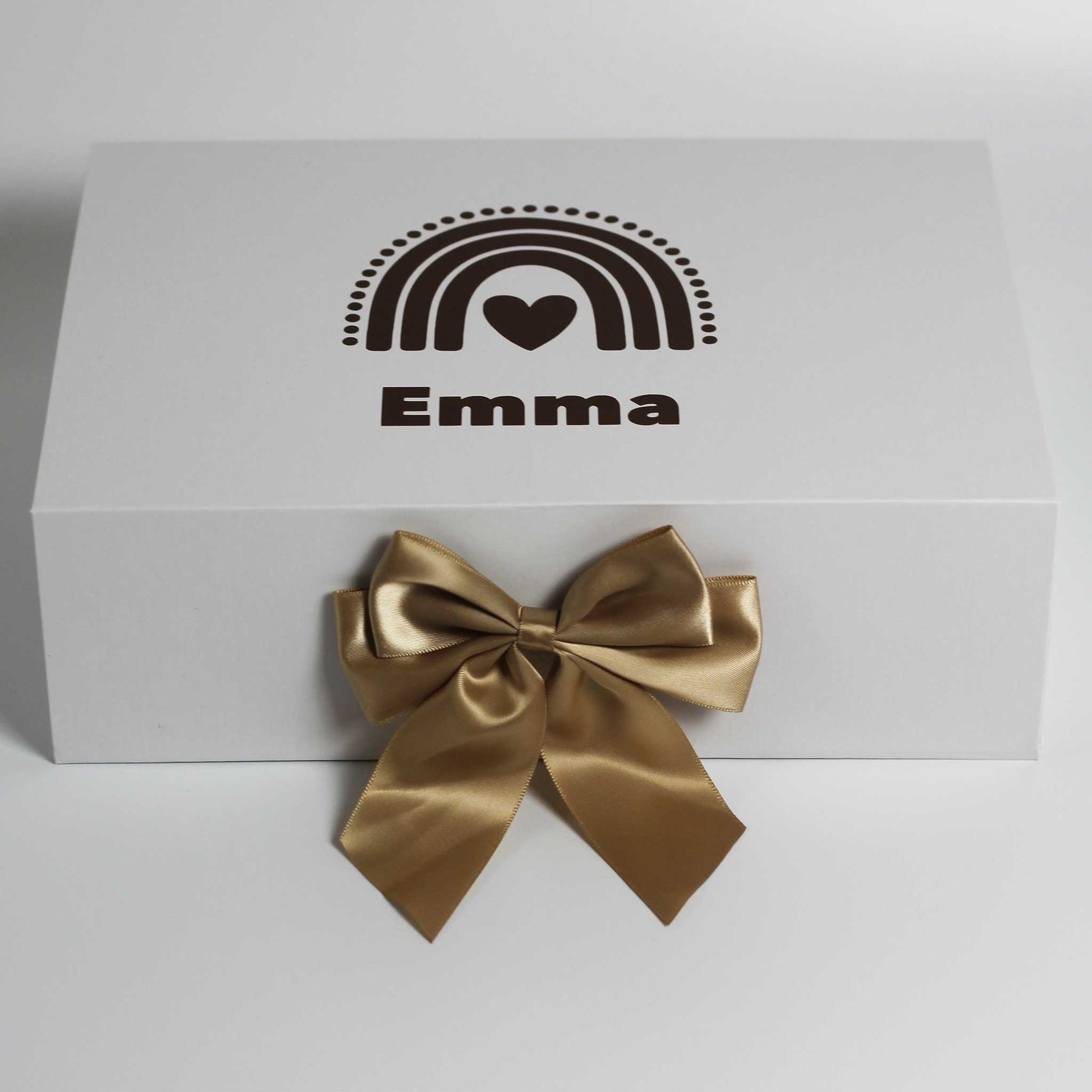 Witte cadeaudoos met een regenboog in donkere tinten en de naam Emma op de deksel, met een grote glanzende gouden strik aan de voorkant op een witte achtergrond