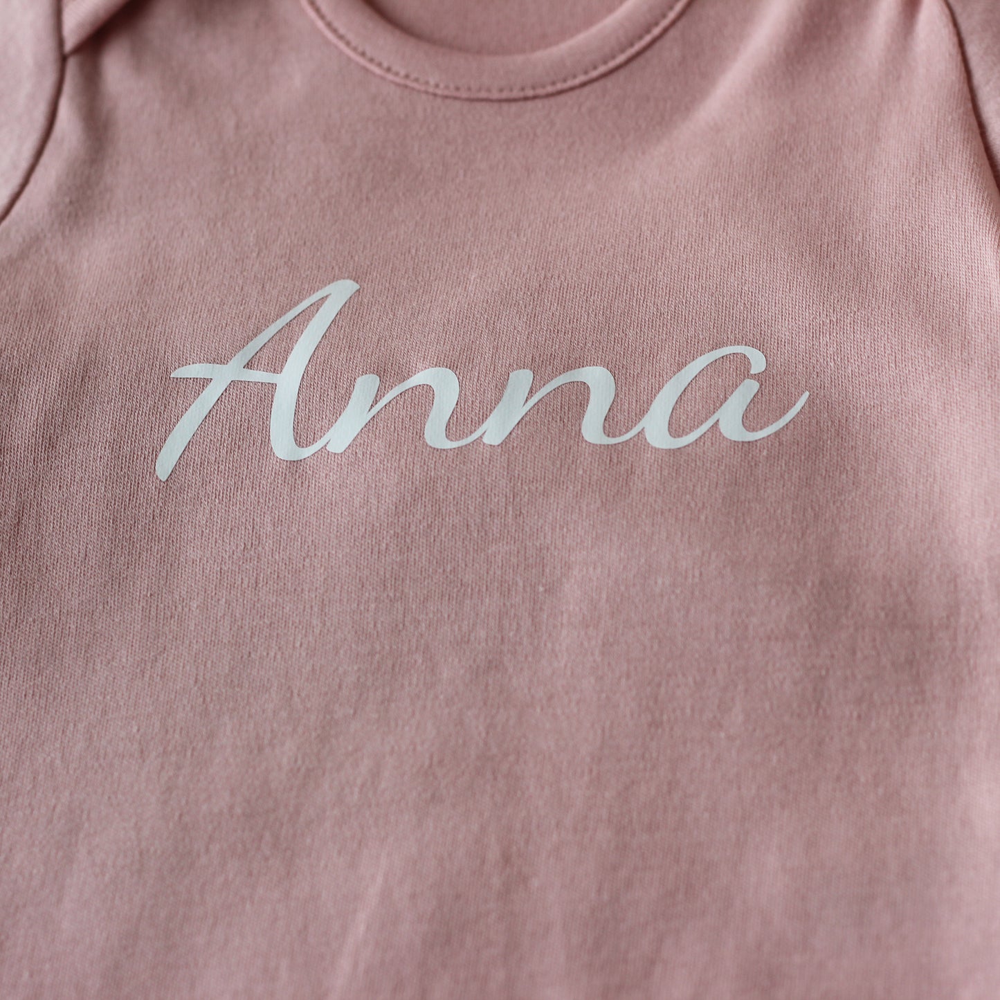 Detail van de naam Anna op een roze babyrompertje
