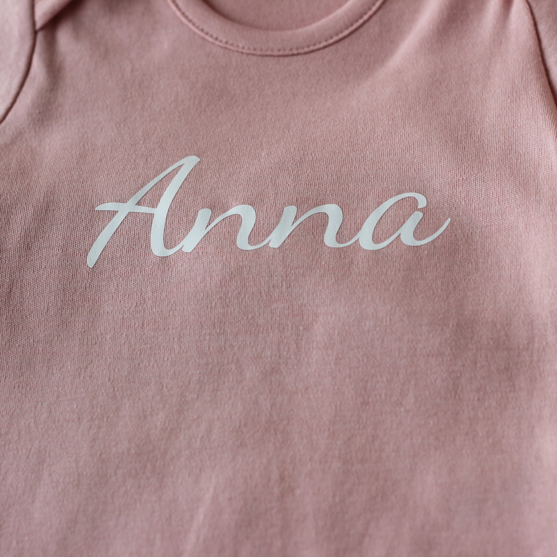 Detail van de naam Anna op een roze babyrompertje