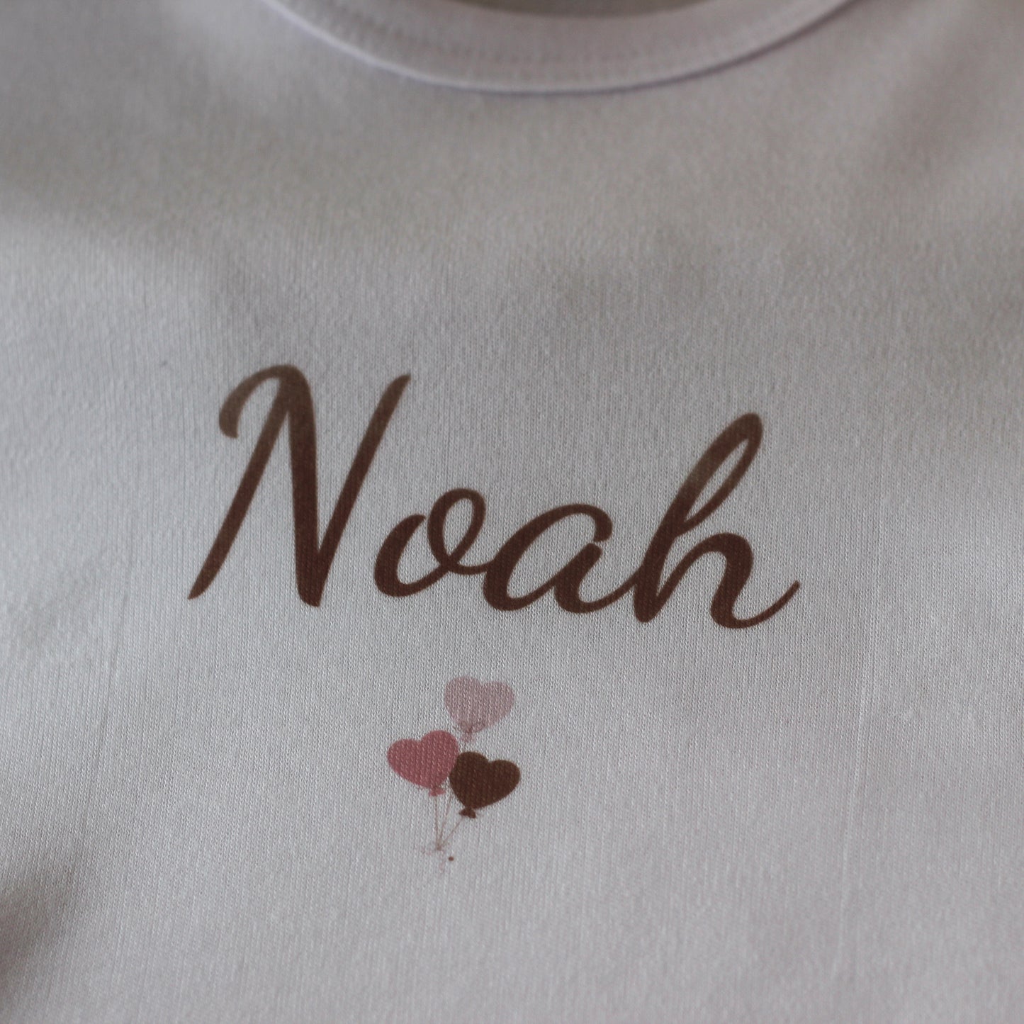 Detail van wit rompertje met naam Noah en drie kleine ballonnen in blush tinten