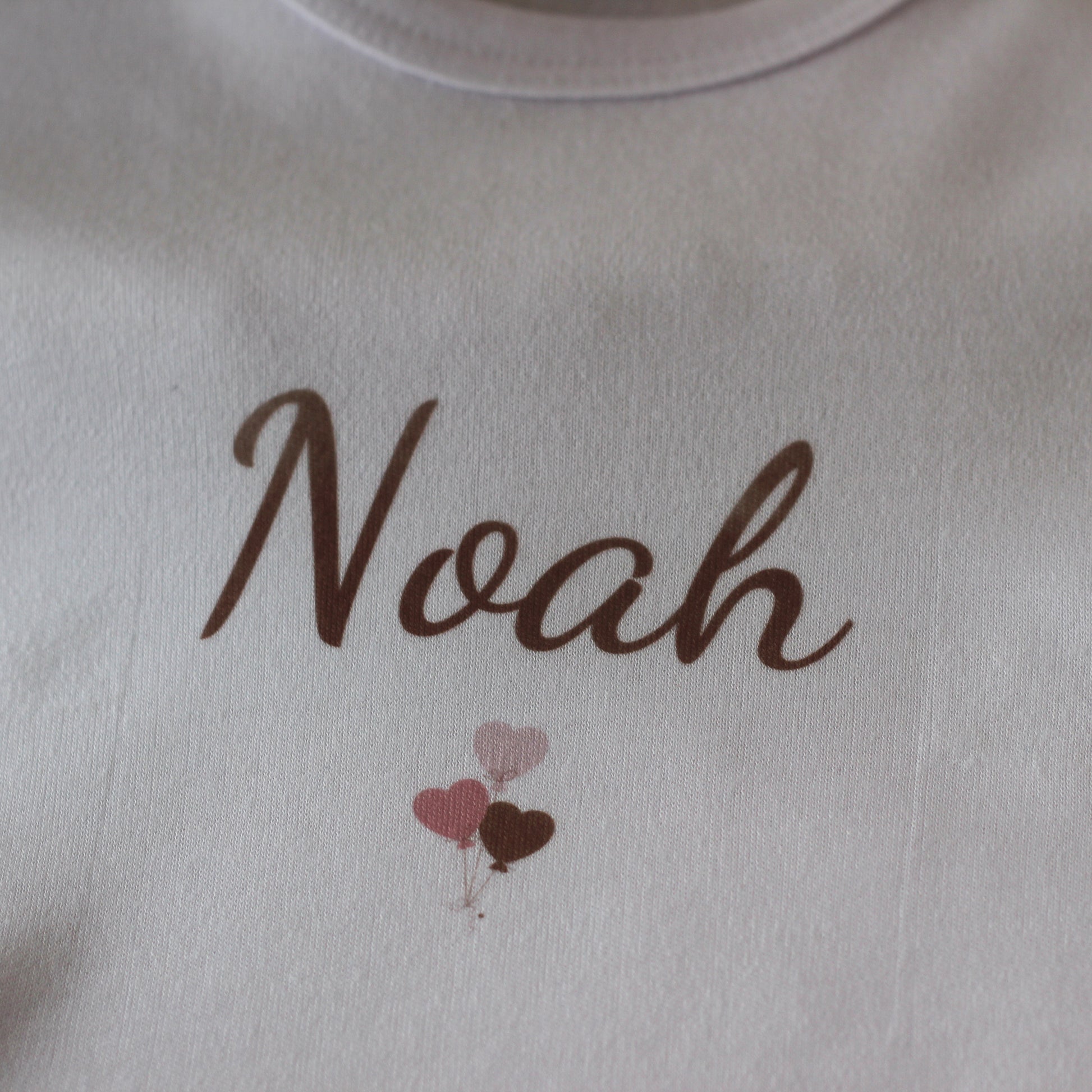 Detail van wit rompertje met naam Noah en drie kleine ballonnen in blush tinten