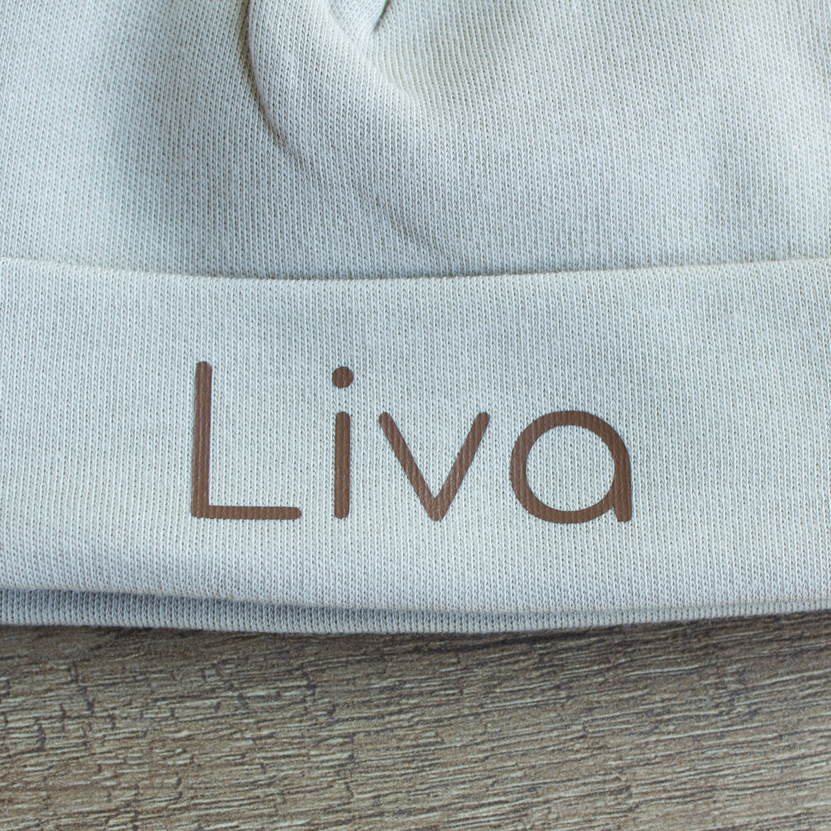 Close-up van gepersonaliseerd Sandstone Grey babymutsje met de naam Liva in chocoladebruine letters