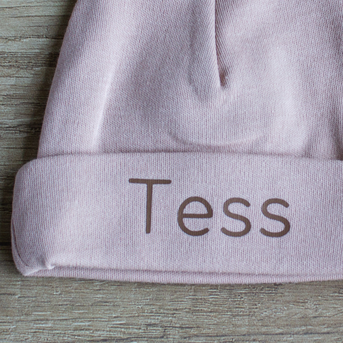 Close-up van gepersonaliseerd Pinkstone babymutsje met de naam Tess in chocoladebruine letters