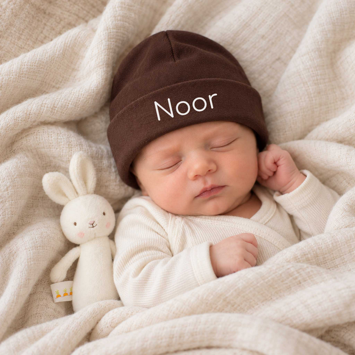 Slapende baby met chocoladebruin katoenen babymutsje, gepersonaliseerd met de naam Noor in witte letters.