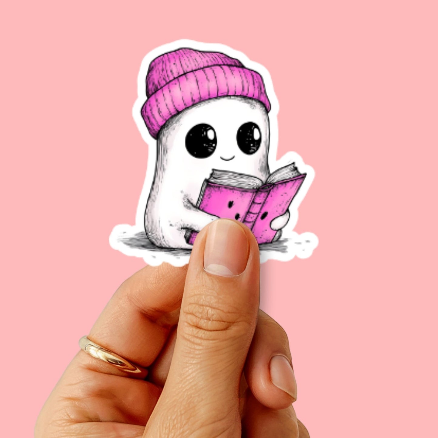 Sticker van een schattig spookje met roze muts en boek, wordt vastgehouden voor een roze achtergrond.