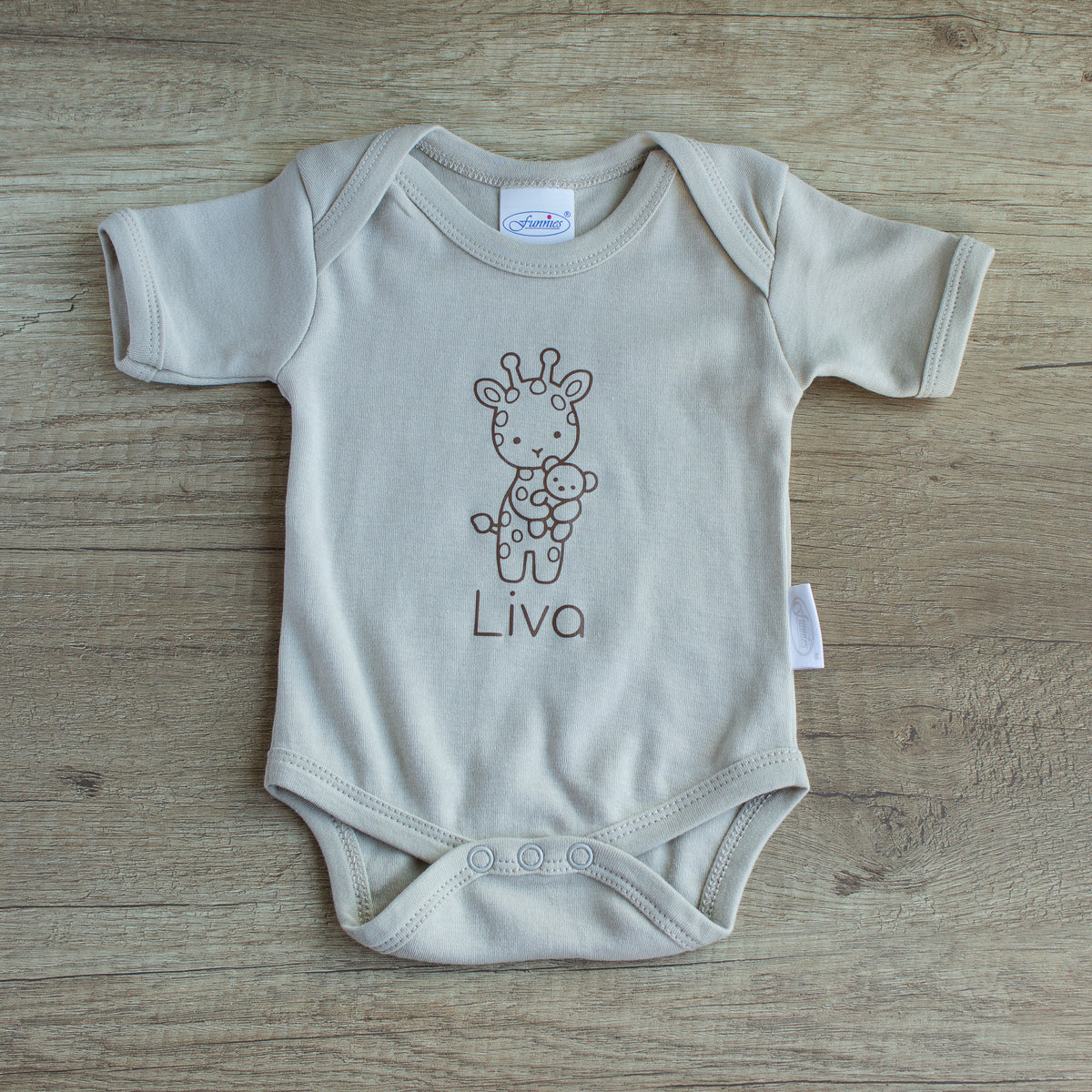 Gepersonaliseerd newborn rompertje in Sandstone Grey met girafje en de naam Liva in chocoladebruin, liggend op een houten tafel.