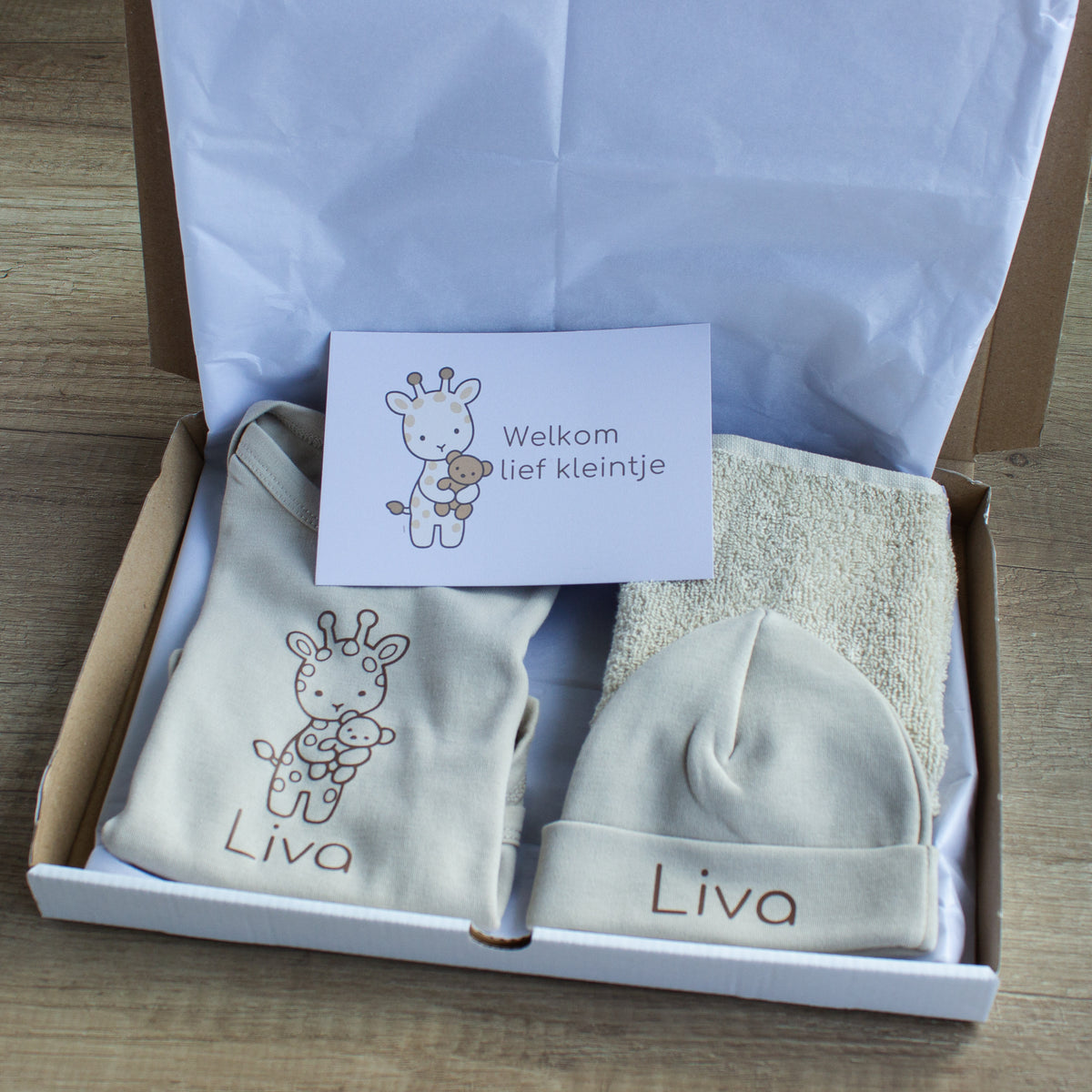 Open newborn cadeauset Girafje in zandkleur met gepersonaliseerde romper en muts met naam Liva, spuugdoekje en kaartje ‘Welkom lief kleintje’.