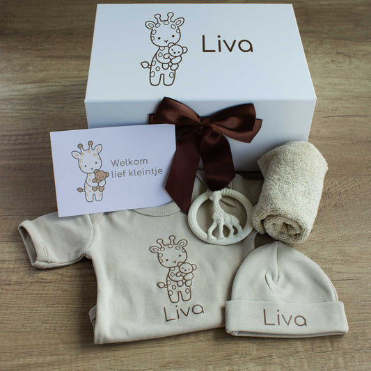 Naturel babycadeauset met een gepersonaliseerde ecru romper en muts met de naam Liva. Achter de kleding staat een witte cadeaudoos met een getekend girafje en de naam Liva, versierd met een chocoladebruine strik. Bij de set liggen een crèmekleurige bijtring in de vorm van een giraf, een opgerold ecru spuugdoekje en een kaart met een girafje en de tekst ‘Welkom lief kleintje’.