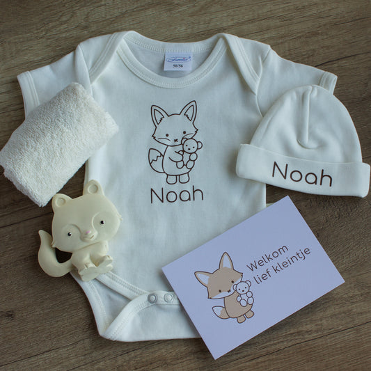 Inhoud van de luxe baby giftbox met vosje in ecru: gepersonaliseerd rompertje en mutsje met de naam Noah en vosillustratie, zacht ecru spuugdoekje, crèmekleurig vosje als bijtspeeltje en een kaart met de tekst ‘Welkom lief kleintje’, gefotografeerd op een houten ondergrond.