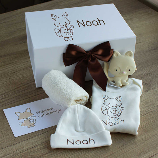 Luxe babycadeauset met vosje in ecru, met een gepersonaliseerde romper en muts met de naam Noah, een crèmekleurig vosje als bijtspeeltje, een ecru spuugdoekje en een kaart met de tekst ‘Welkom lief kleintje’. Achter de producten staat de witte luxe cadeaudoos met vosillustratie en naam Noah, afgewerkt met een chocoladebruine satijnen strik.