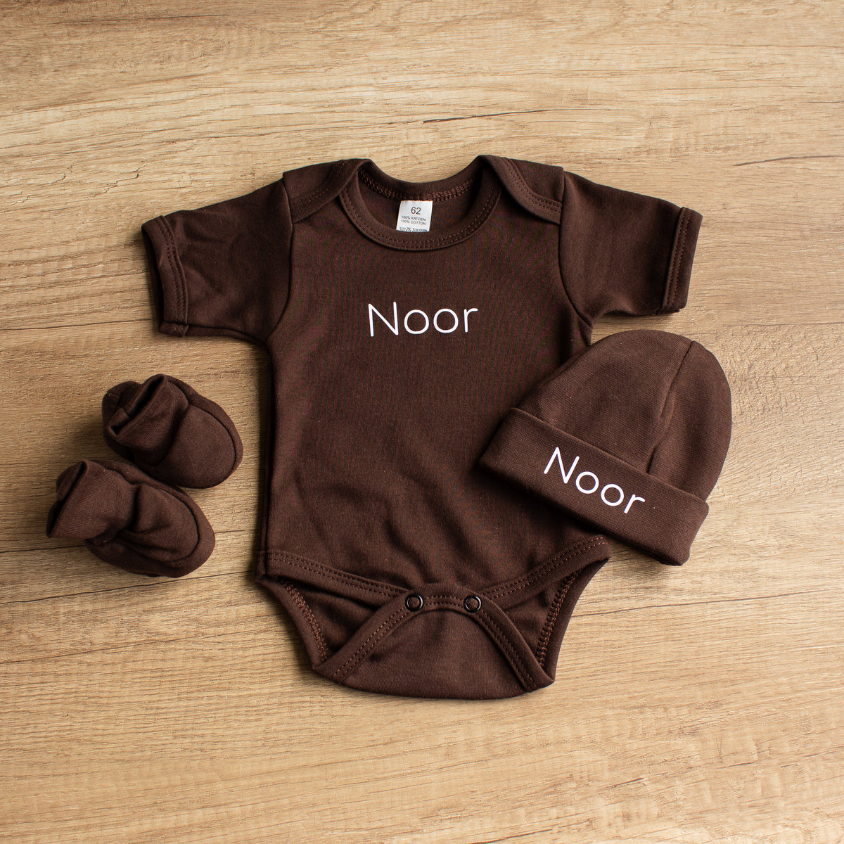 Chocoladebruin babyrompertje met naam Noor, bijpassend gepersonaliseerd mutsje en effen babyslofjes