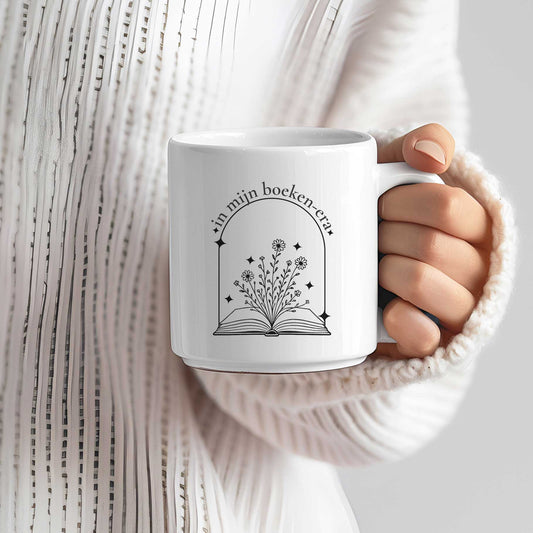 Persoon houdt mok vast met quote “in mijn boeken-era” en illustratie van open boek met bloemen