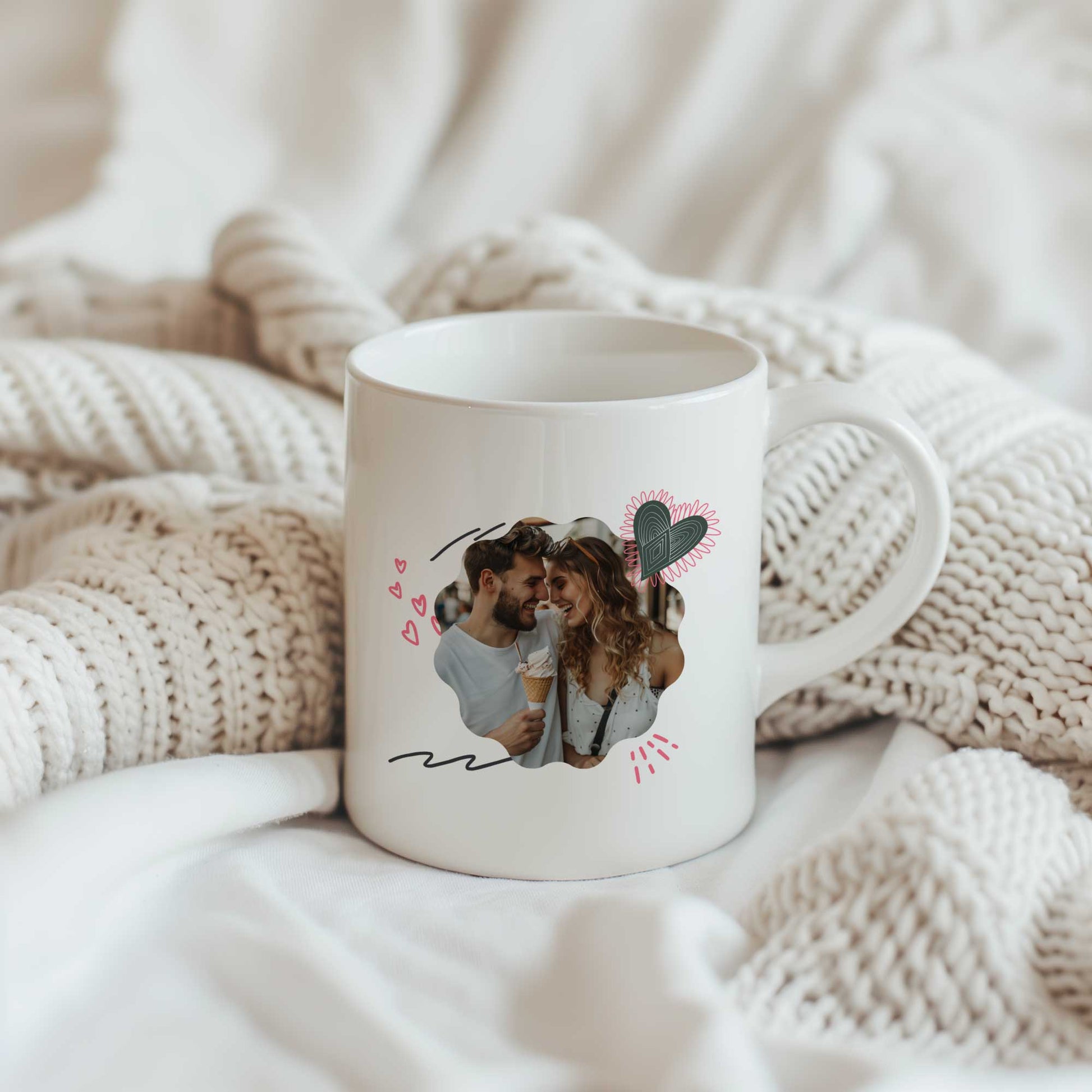 Witte mok met foto van een stel, omringd door getekende hartjes en liefdevolle accenten, geplaatst op een beige gebreide deken