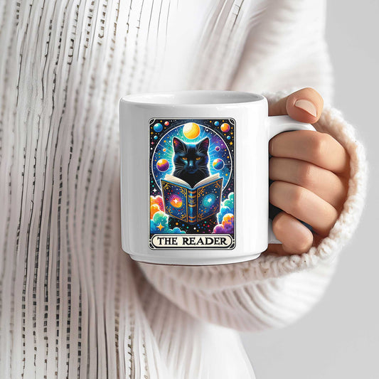 Hand houdt mok met zwarte kat tarotdesign vast, kleurrijke planeten en kosmos, tekst The Reader