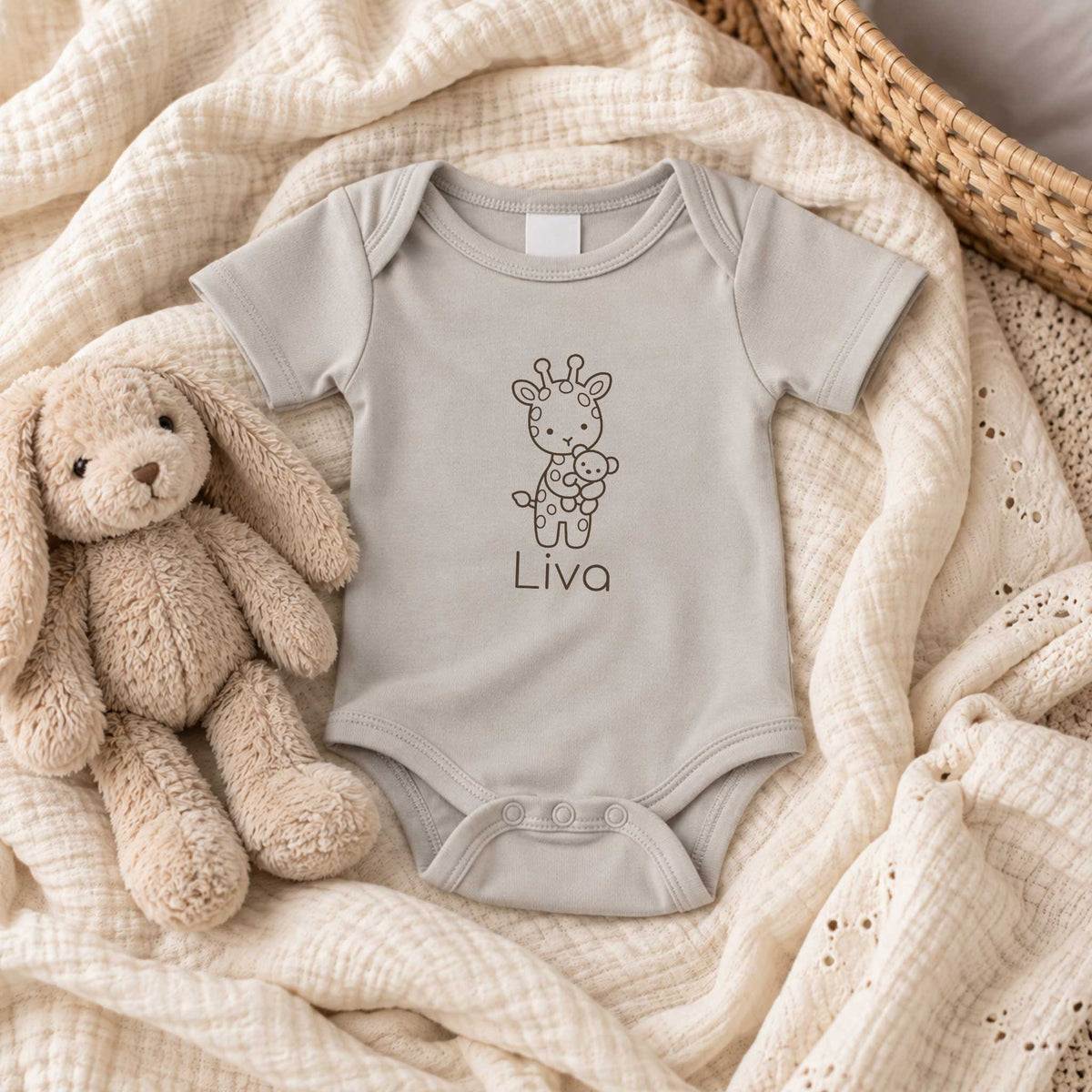 Sandstone Grey babyromper met gepersonaliseerde giraf en naam, liggend op zachte lichte stoffen naast een beige knuffel