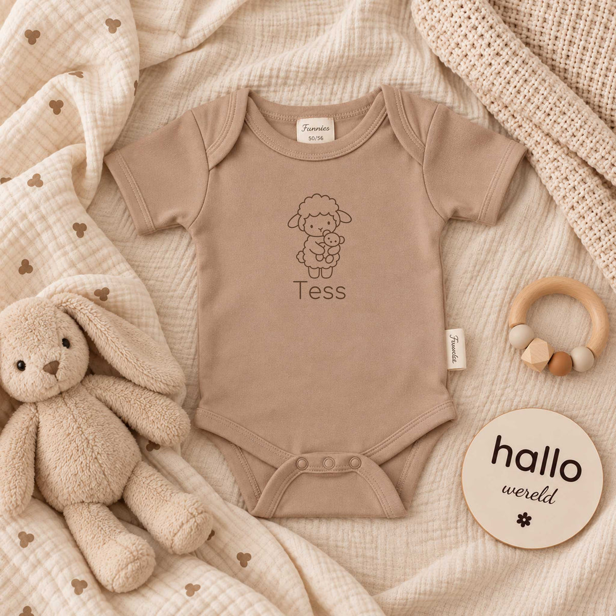 Pinkstone babyromper met gepersonaliseerd lammetje en naam, liggend tussen zachte beige dekens met knuffel en houten accessoires