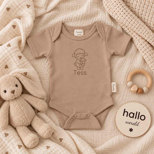 Pinkstone babyromper met gepersonaliseerd lammetje en naam, liggend tussen zachte beige dekens met knuffel en houten accessoires