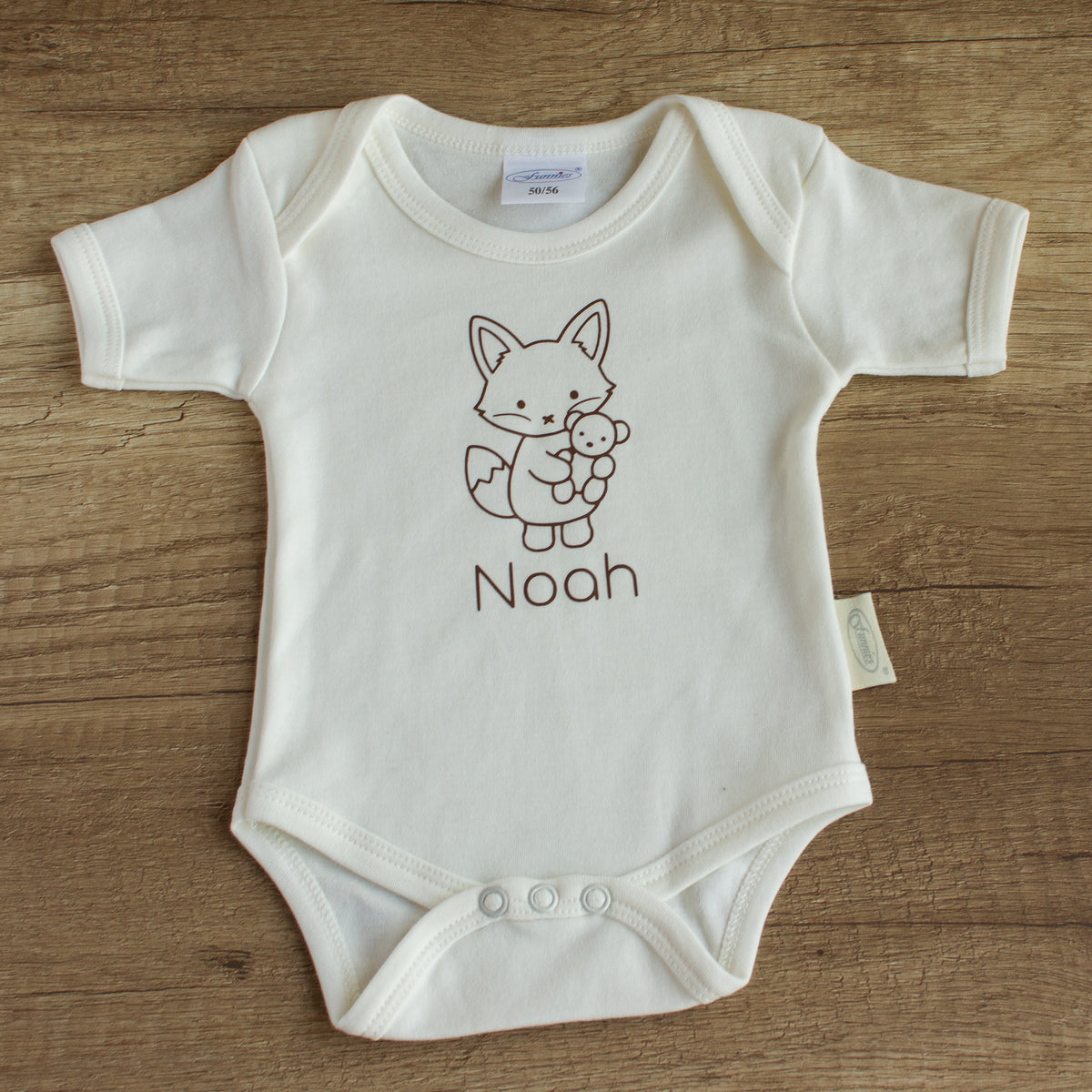 Ecru babyromper met vosje en gepersonaliseerde naam, liggend op een houten tafel