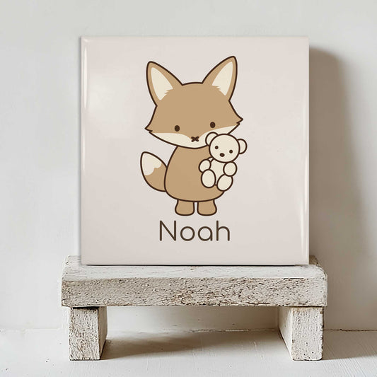 Vierkant keramisch tegeltje met een vosje dat een beertje vasthoudt en de naam Noah, staand op een wit houten krukje.