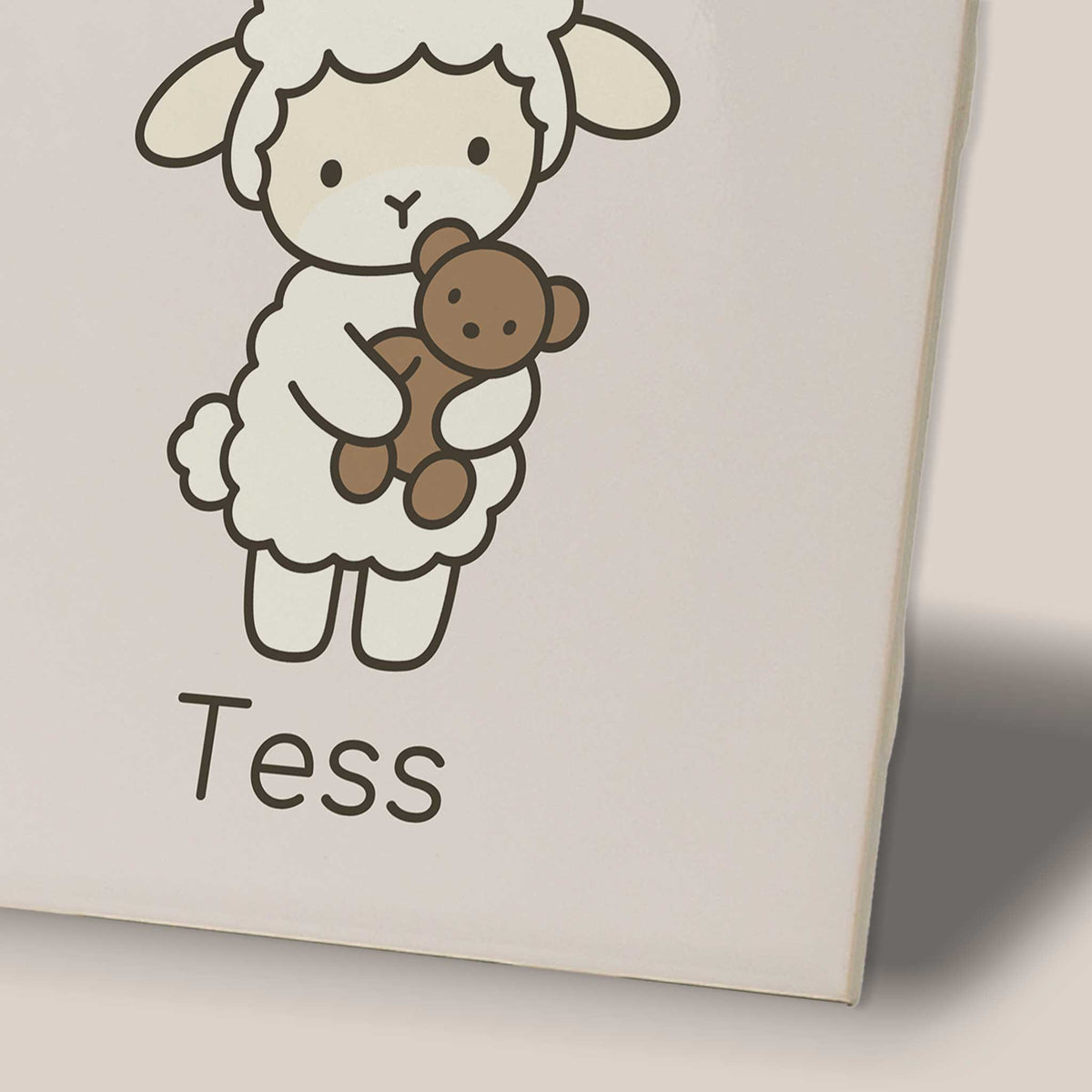 Close-up van een keramisch tegeltje met een lammetje dat een beertje vasthoudt en de naam Tess.