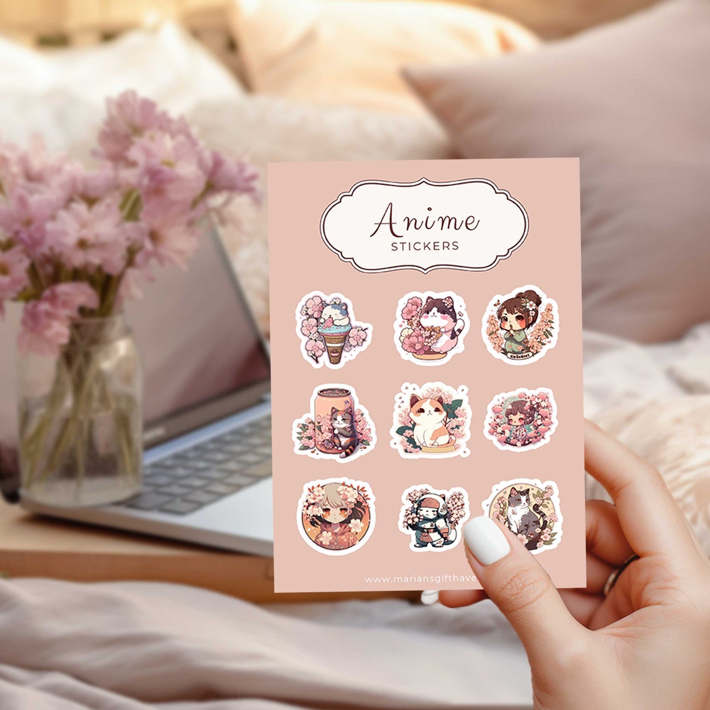 Anime stickervel met kersenbloesemthema, vastgehouden voor een laptop en bloemenvaas op een bed.