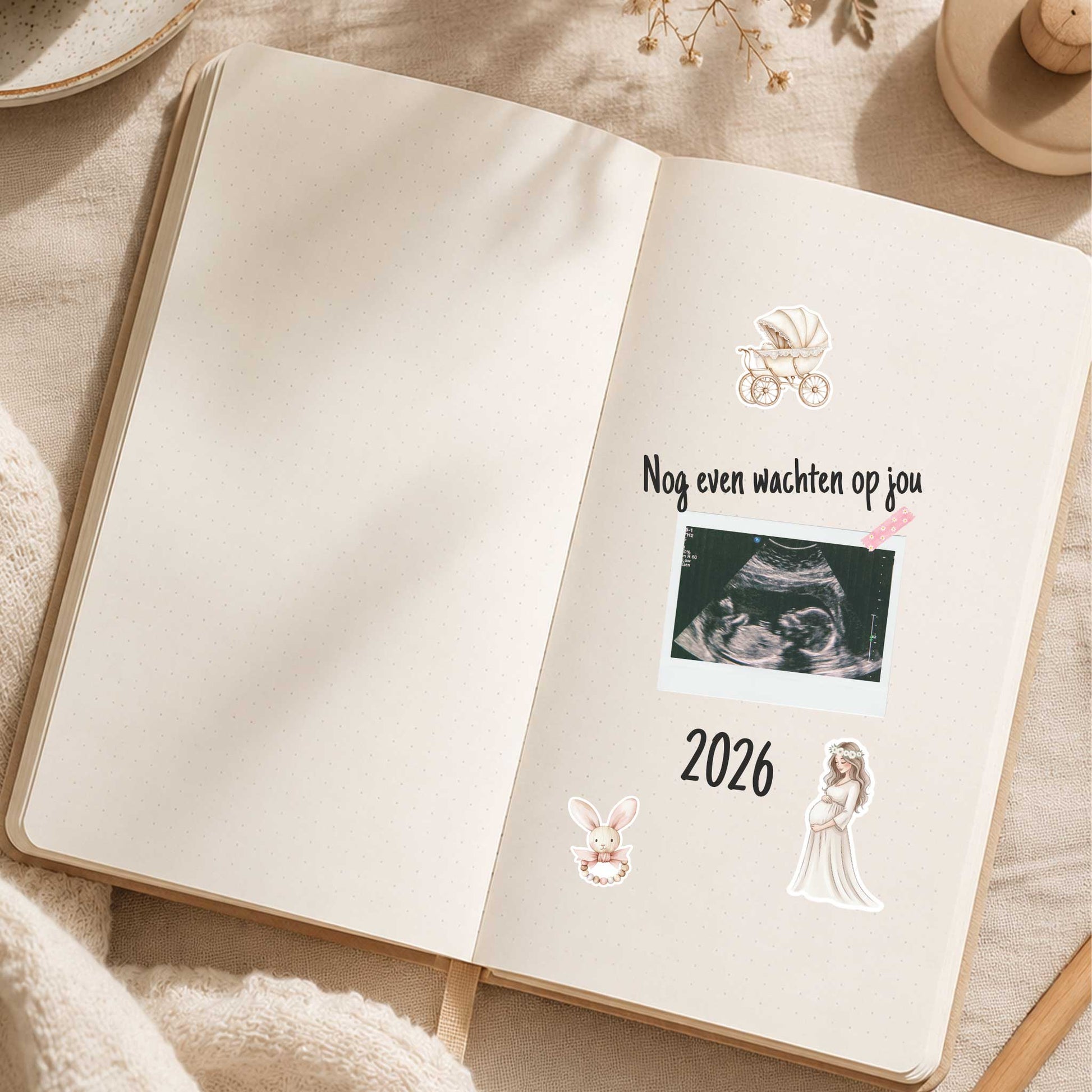 Open zwangerschapsdagboek met een echofoto, de tekst 'Nog even wachten op jou' en Baby Dromen stickers van een kinderwagen, konijntje en zwangere vrouw op een beige ondergrond.