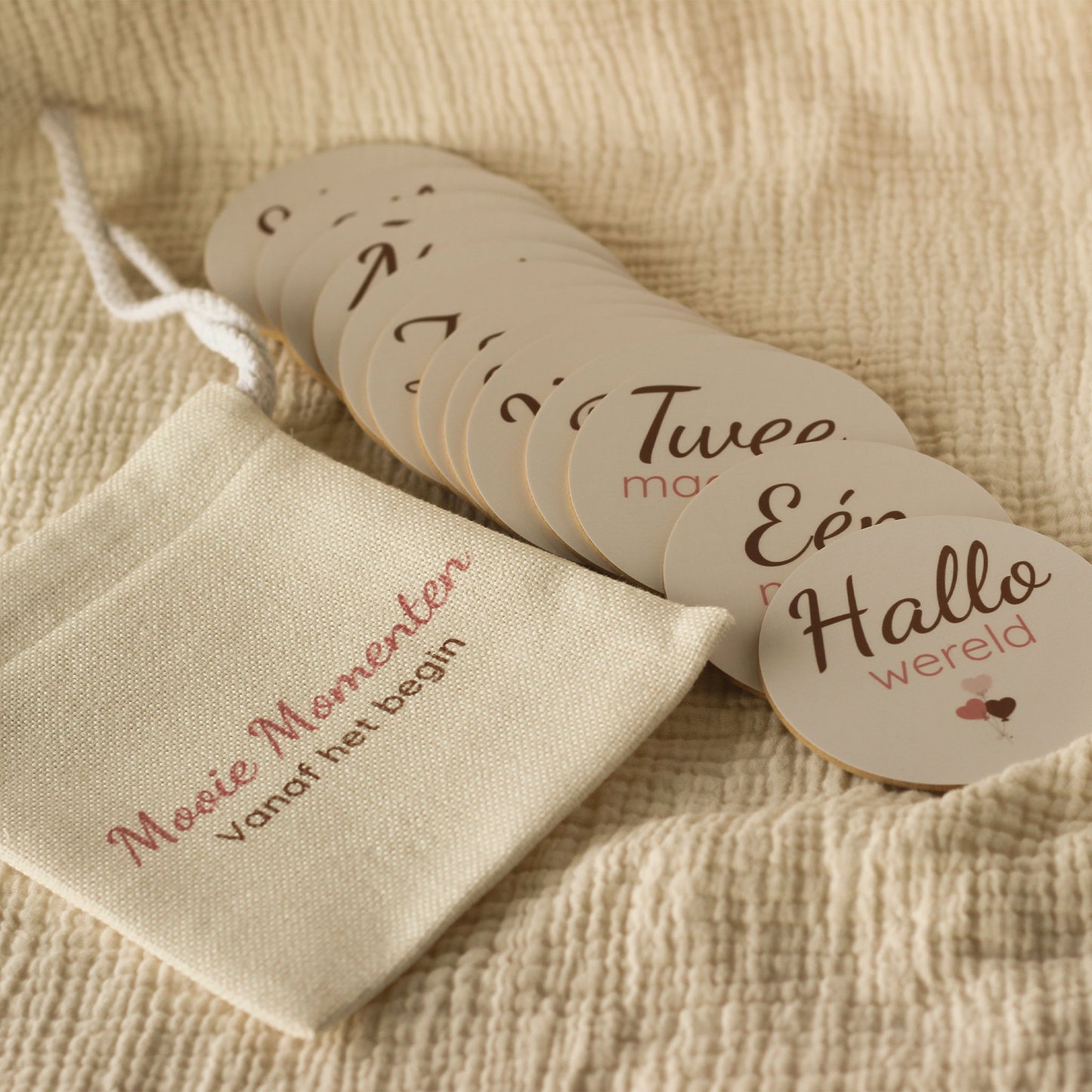Set baby mijlpaalschijfjes voor het eerste levensjaar in een linnen cadeauzakje op een zachte beige stof