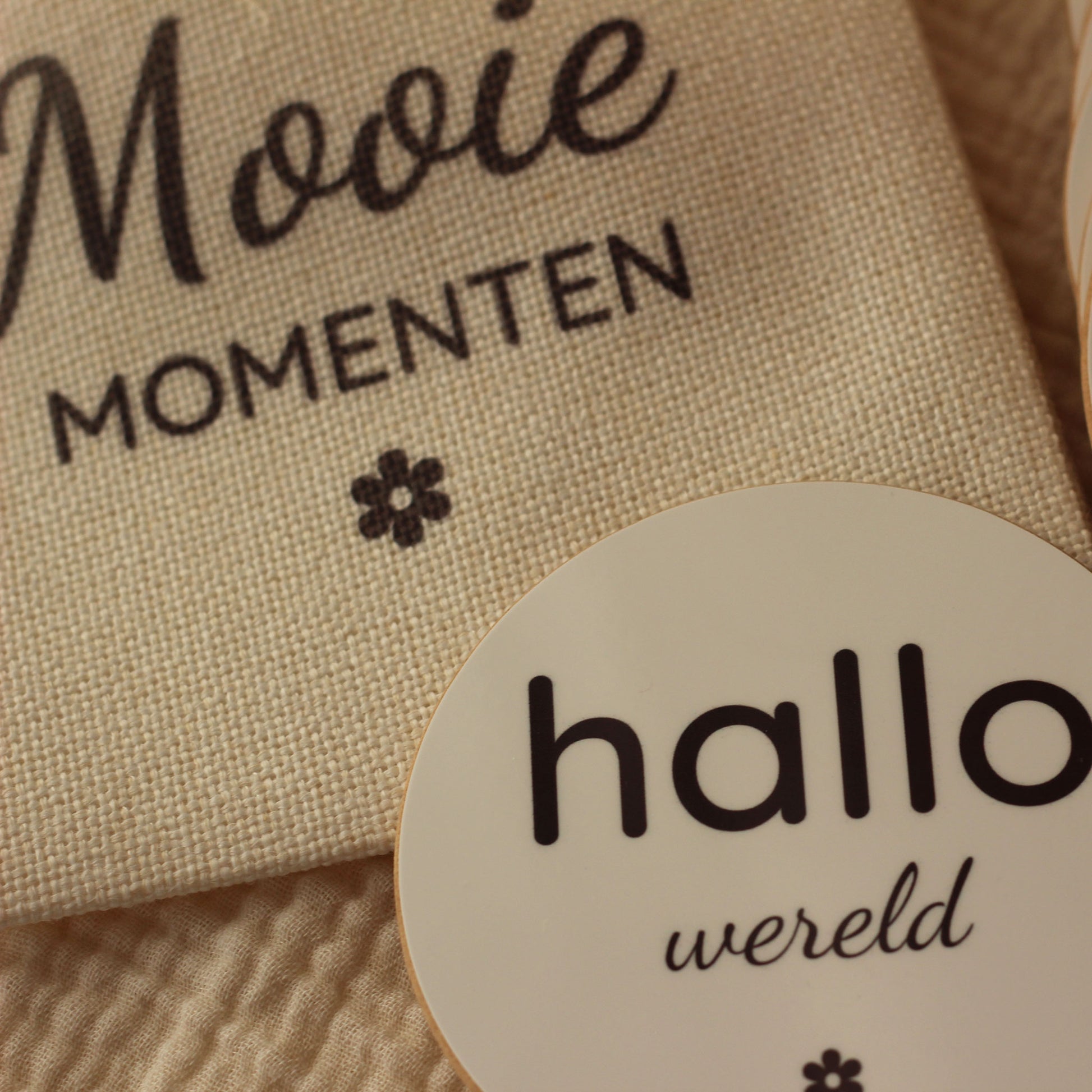 Close-up van een ronde mijlpaalschijf met de tekst “hallo wereld” naast een linnen zakje met tekst “Mooie momenten”.