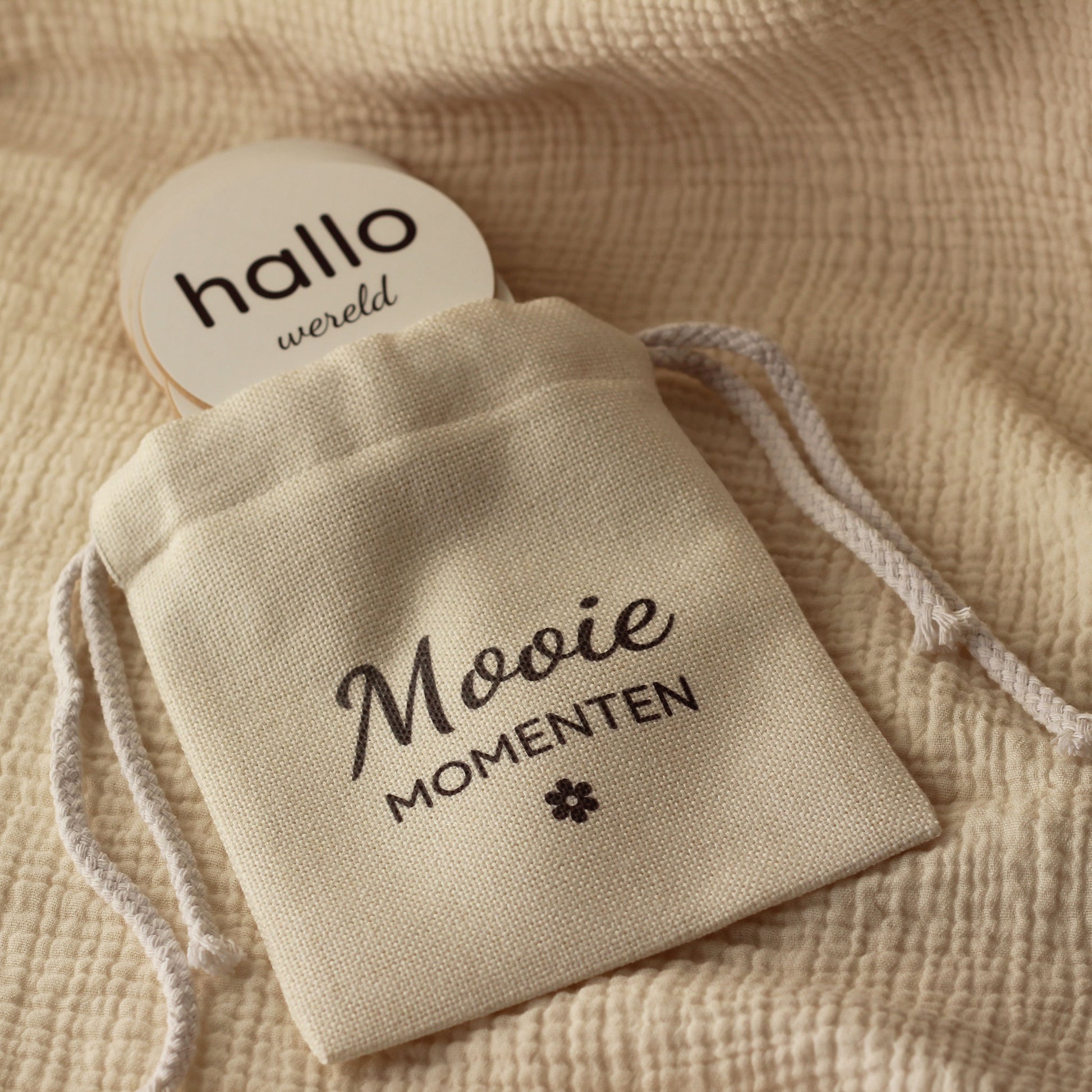 Linnen zakje met tekst “Mooie momenten” met een ronde mijlpaalschijf met de tekst “hallo wereld”.
