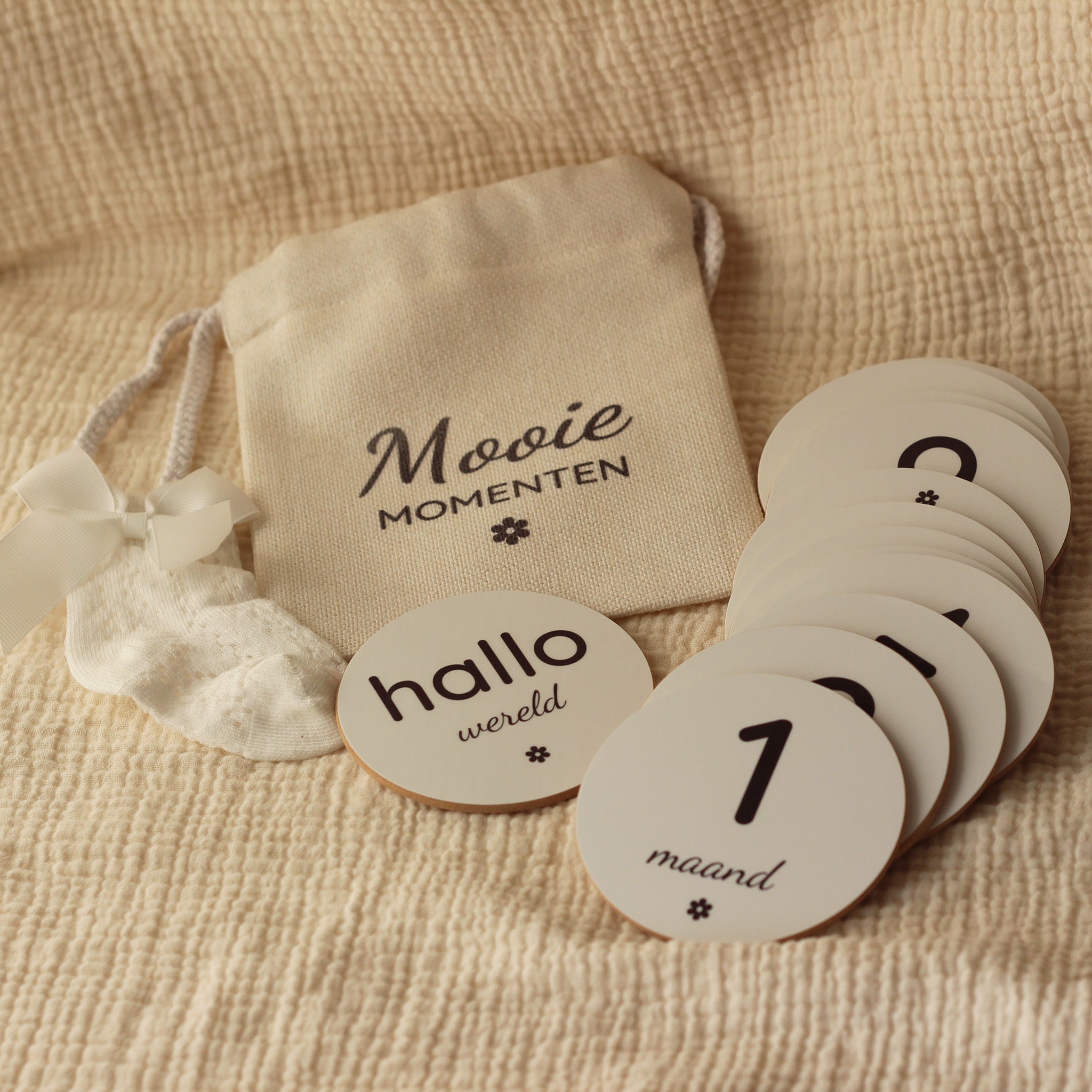 Set ronde baby mijlpaalschijfjes met linnen zakje op een beige mousseline doek.