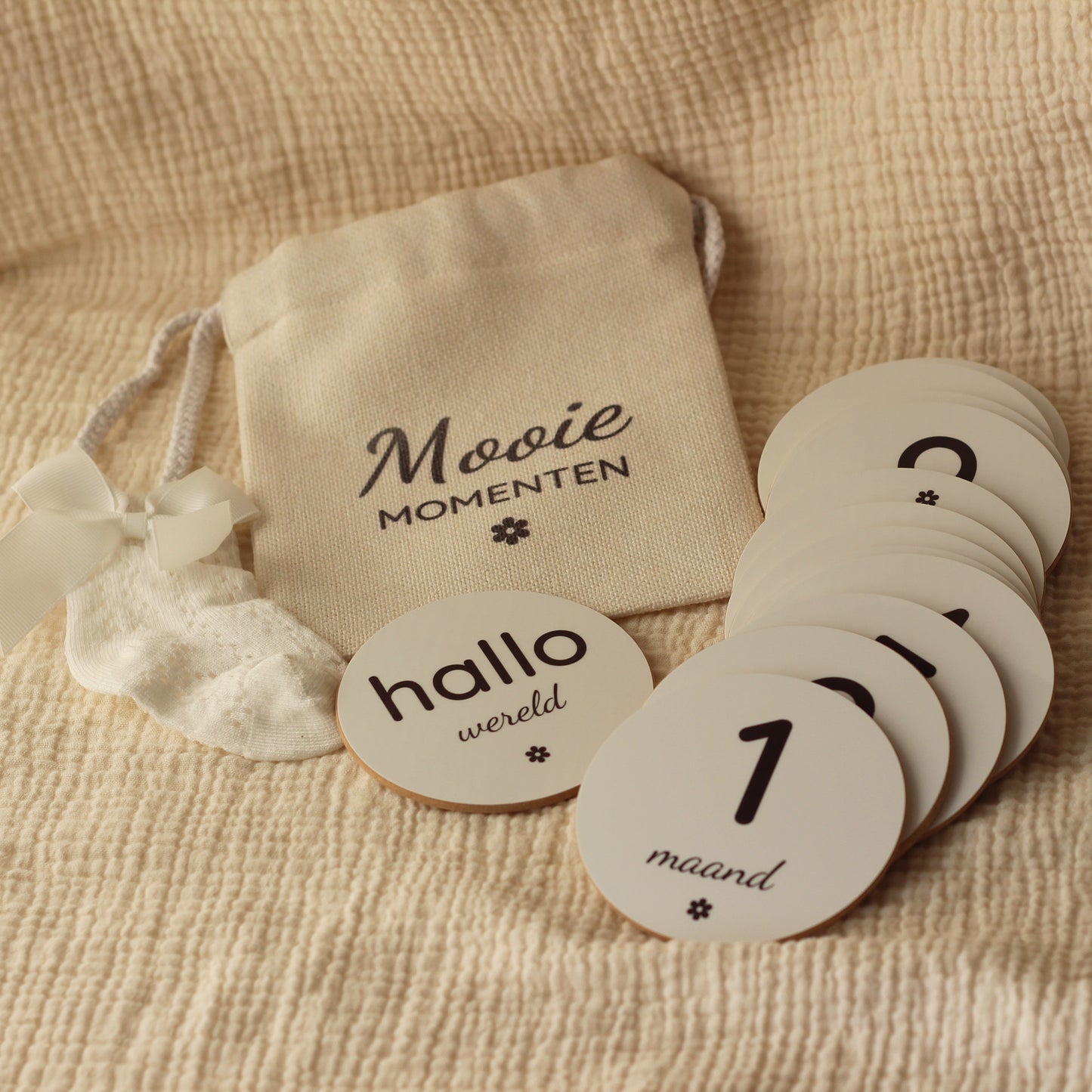 Set ronde baby mijlpaalschijfjes met linnen zakje op een beige mousseline doek.